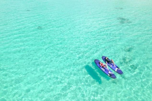 リゾートバイトの休日に海で遊ぶイメージ画像。透き通ったエメラルドグリーンの海で、2人がSUPの上に寝そべっている様子。
