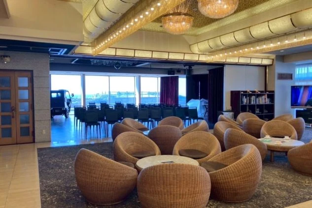 ホテルや旅館のロビーの画像。落ち着いた照明で、ゆったりとくつろげる空間。ラタン製のソファが並んでおり、奥には窓から光が差し込む広々としたスペースが。ホテルの共有スペースの画像。