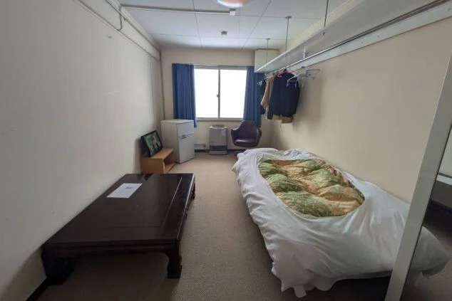 リゾートバイトの寮の部屋の画像。部屋には布団と小さなテーブル、冷蔵庫が置かれている。窓際にはヒーターが置かれており、寒い季節にも快適に過ごせる。リゾートバイトの寮の部屋の画像。