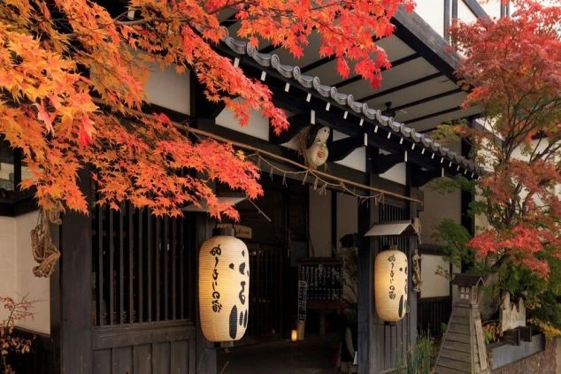 紅葉に彩られた旅館の玄関の画像。軒下には大きな提灯が2つ吊り下げられており、和の情緒あふれる落ち着いた雰囲気が伝わってくる。リゾートバイトのホテルや旅館の風景の画像。