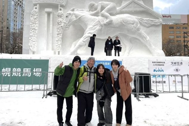 4人の若い男女が笑顔でカメラに向かってポーズをとる画像。札幌雪まつりの会場であることがわかる。リゾートバイトを通じてできた友人たちと休日に観光を楽しんでいるワクトリスタッフの画像。
