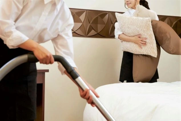 ホテルや旅館の清掃をしている女性スタッフ2人の画像。一人は掃除機をかけ、もう一人はベッドのシーツや枕を整えている。リゾートバイトの仕事内容の一つである、客室清掃の仕事風景の画像。