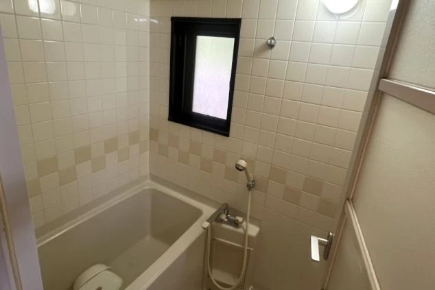 リゾートバイトの寮のバスルームの画像。白いタイル張りの壁に浴槽とシャワーが備え付けられ、窓が付いている。リゾートバイトの寮の風呂場の画像。