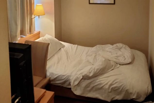 リゾートバイトの寮の部屋にあるベッドの画像。清潔な白い布団がかけられており、枕元にはスタンドライトが置かれている。リゾートバイトの寮の部屋の画像。