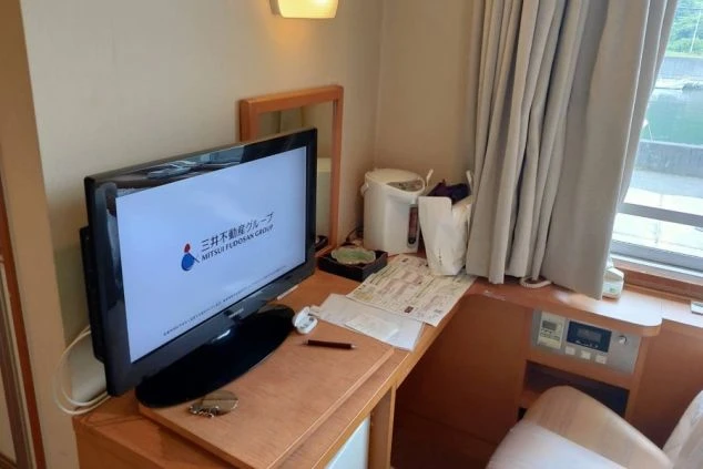 リゾートバイトの寮の部屋にあるデスク周りの画像。テレビ、電気ケトル、書類などが置かれ、窓からは海が見える。リゾートバイトの寮の部屋の画像。