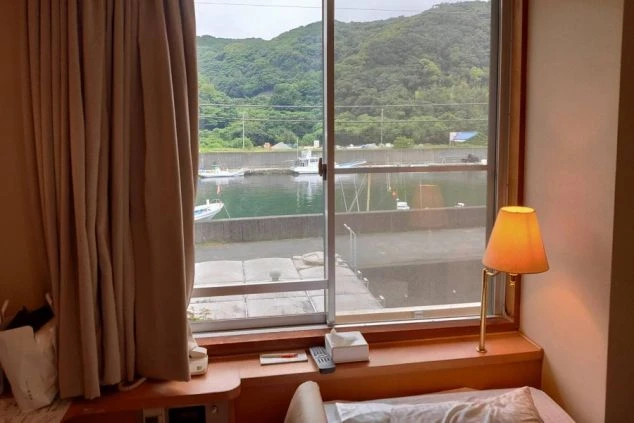 リゾートバイトの寮の部屋の窓からの景色を写した画像。窓の外には漁港と緑の山々が見え、海沿いのリゾート地であることがわかる。リゾートバイトの寮の部屋の画像。