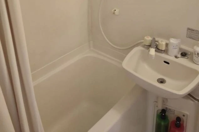 リゾートバイトの寮に備え付けられたバスタブと洗面台の画像。白い浴槽にシャワーカーテンがかけられており、清潔感がある。リゾートバイトの寮の風呂場の画像。