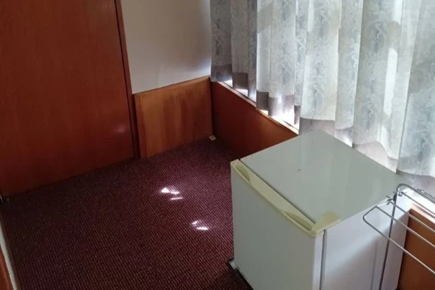 寮の個室。小型冷蔵庫と物干しラック、窓にカーテンが映る。