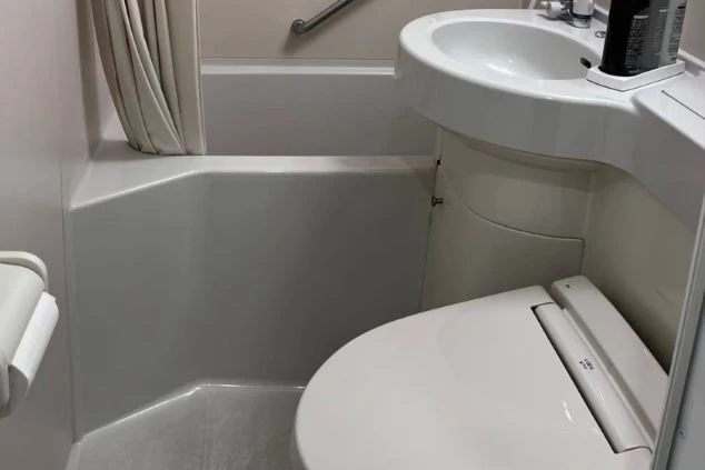 寮の個室。小型冷蔵庫と物干しラック、窓にカーテンが映る。