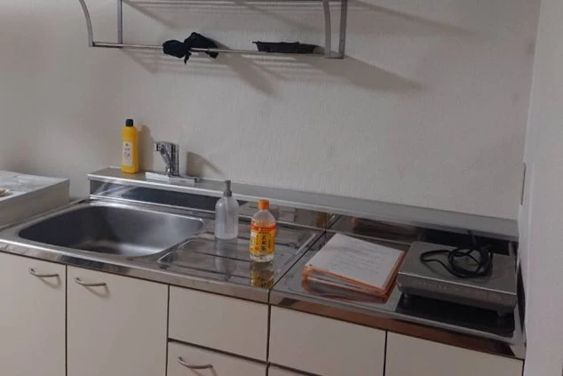 リゾートバイトの寮のキッチンを写した画像。白い壁と棚、ステンレス製のシンクがあり、IHコンロが備え付けられている。リゾートバイトの寮の共用キッチンの画像。