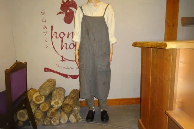 カフェで着用されている制服の画像。白いブラウスに、グレーのロングエプロンとパンツを合わせた、おしゃれな制服である。リゾートバイトの仕事内容を表す、制服の画像。