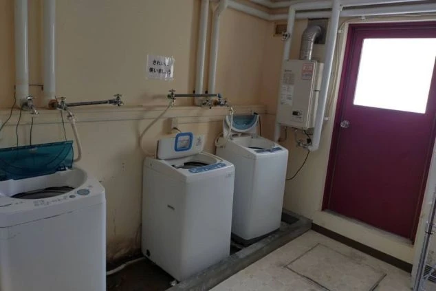 リゾートバイトの寮に備え付けられた洗濯機を撮影した画像。上から洗濯物を入れる縦型タイプが2台設置されている。リゾートバイトの寮の共用スペースの画像。