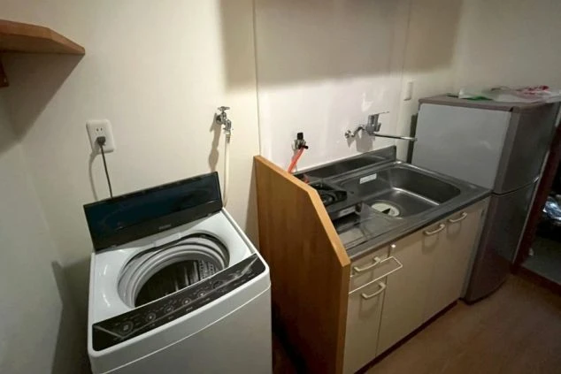 リゾートバイトの個室寮にあるミニキッチンと洗濯機。冷蔵庫、ガスコンロも備え付けられ、自炊や生活に便利な設備の画像。