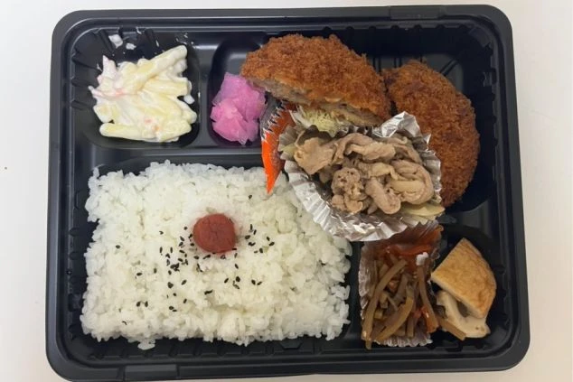 ご飯、メンチカツ、豚肉の生姜焼き、マカロニサラダなどが詰められたお弁当形式のまかない画像。