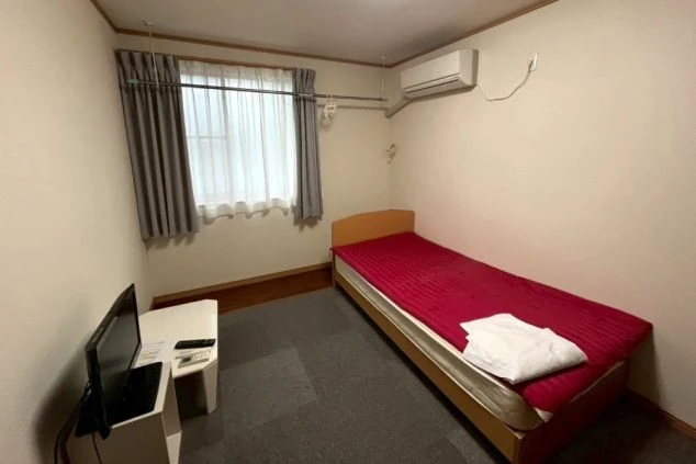 リゾートバイトの個室寮の室内。シングルベッド、テレビ、エアコンが備え付けられており、プライベート空間が確保されたシンプルな寮の部屋の画像。
