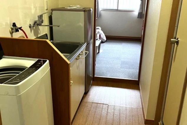 リゾートバイトの個室寮の入口付近。ミニキッチンと洗濯機、冷蔵庫が見え、奥には部屋が広がる、住み込み生活の雰囲気が伝わる寮の画像。