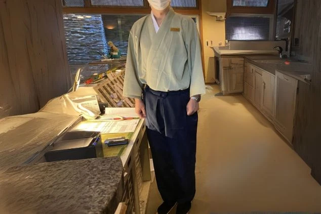 和風の制服を着用した男性スタッフの画像。上下ともにゆったりとしたデザインで、薄い緑色の上着に紺色の前掛けとズボンを合わせている。旅館や和食レストランでのリゾートバイトの仕事内容を表す、制服の画像。