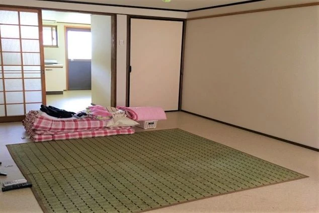 リゾートバイトの個室寮の室内。畳敷きのスペースがあり、布団を敷いてゆっくり休むことができます。手前にはキッチンや玄関が見え、生活しやすい間取りです。