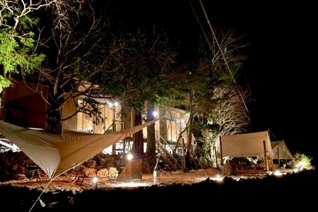 リゾートバイトの休日に観光するイメージ画像。夜のキャンプ場で、ライトアップされたテントや木々が幻想的な風景。
