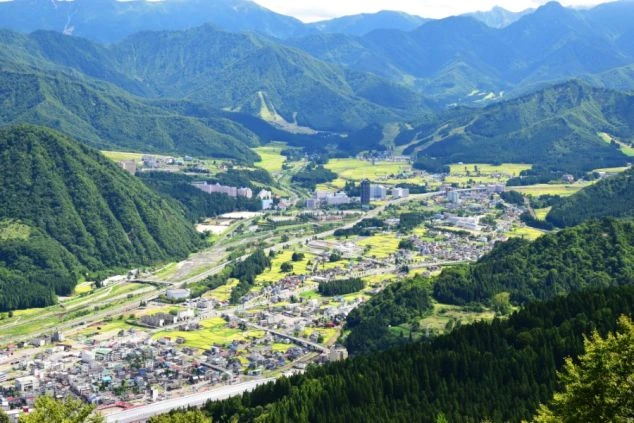 新潟県越後湯沢の街並みを上空から撮影した画像。山々に囲まれた盆地に、ホテルや民家、そして田んぼが広がっている。リゾート地ならではの自然豊かな風景の画像。