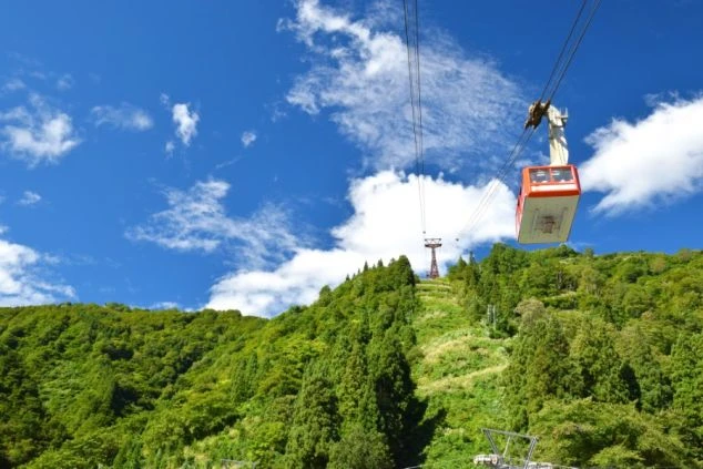 新潟県越後湯沢の緑豊かな山々の上空を、ロープウェイが運行している画像。リゾートバイトの休日に観光を楽しめる、自然の風景の画像
