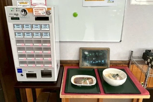 リゾートバイトの食堂に置かれた食券販売機の画像。メニューが書かれた黒板と料理。