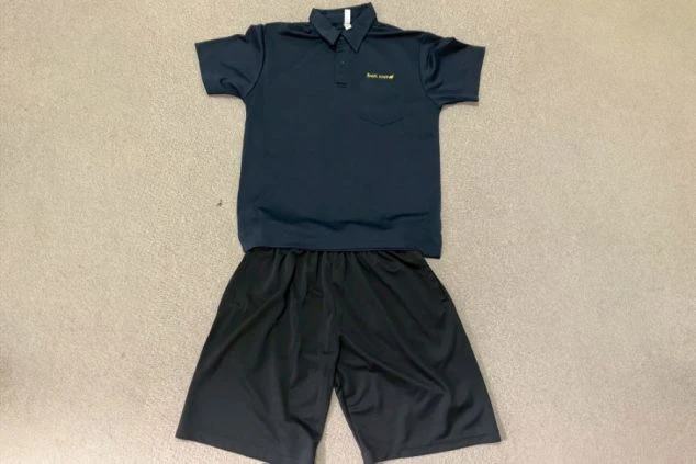 床の上に置かれた、スポーツジムスタッフの制服の画像。濃い紺色のポロシャツと黒いハーフパンツのセットである。リゾートバイトの仕事内容を表す、スポーツジムスタッフの制服画像。