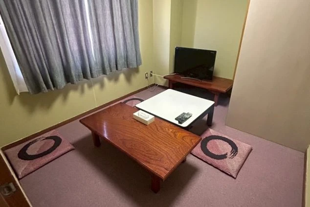 リゾートバイトの寮の部屋の中を撮影した画像。部屋には座布団と2つの座卓、そしてテレビが置かれている。寮の部屋の画像。