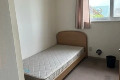 リゾートバイトの寮の個室。ベッド、窓にカーテン、ゴミ箱とカーペットが映る。