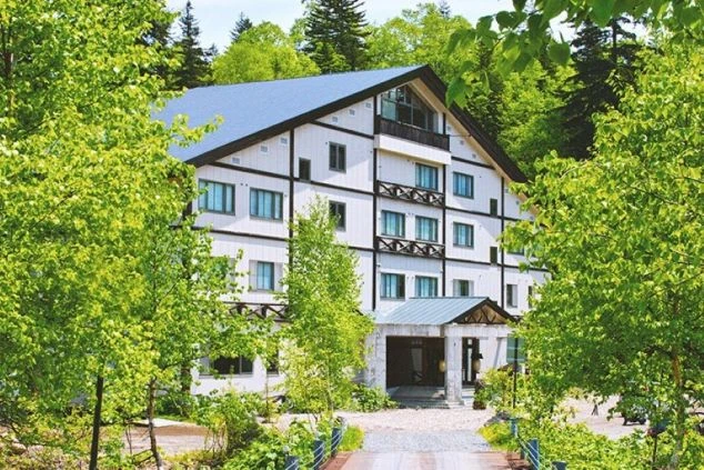 リゾートバイトの勤務先の外観を表現するイメージ画像。新緑の木々に囲まれた、白と黒のコントラストがおしゃれなホテル。