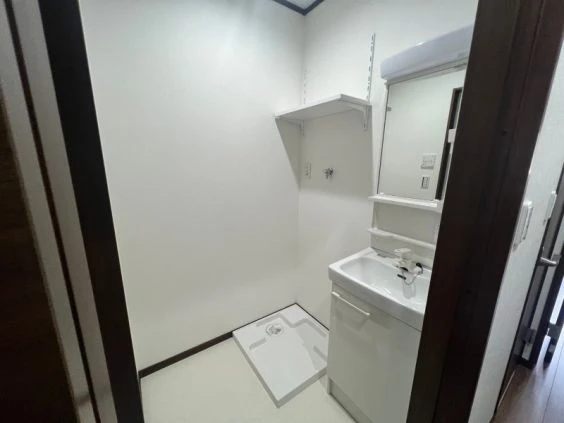 寮の洗面所。洗面台、鏡、棚、洗濯機置き場が映る清潔な空間。