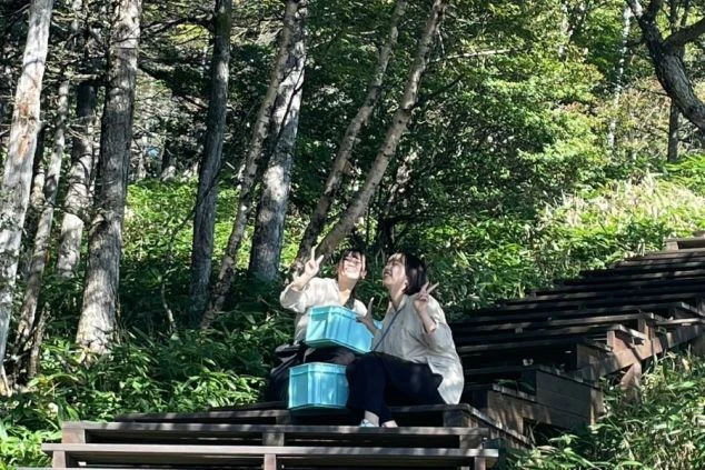 リゾートバイトの休日に観光するイメージ画像。自然の中の階段に座り、楽しそうにピースサインをする女性2人。