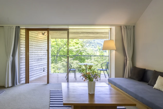 リゾートバイトの社員寮の部屋を表現するイメージ画像。窓の外にバルコニーが見える、ソファが設置された広々とした洋室。