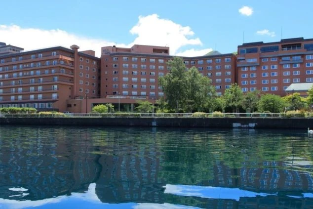 湖畔に建つホテルの外観の画像。建物が水面に反射しており、美しい景色が広がっている。リゾートバイトの仕事場となる、ホテルの外観の画像。