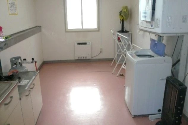 リゾートバイトの個室寮の共用部の画像。洗濯機・乾燥機・キッチンが見える。