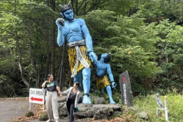 森の中にある大きな鬼の像の前で、楽しそうに記念撮影をする女性2人組の写真。