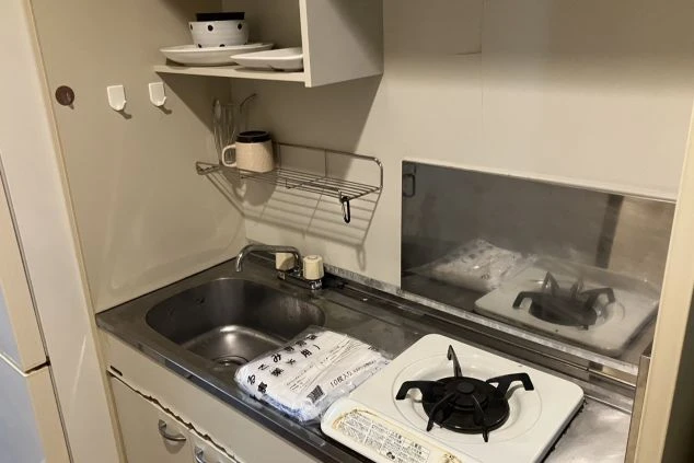 リゾートバイトの寮に備え付けられたコンパクトなキッチン。ガスコンロとシンクがあり、自炊ができるため食費を節約したい求職者に魅力をアピールする画像。