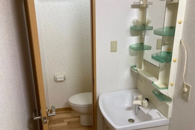 リゾートバイトの寮の洗面台とトイレの画像。コンパクトな洗面台と鏡、隣にはトイレのドアが見える。