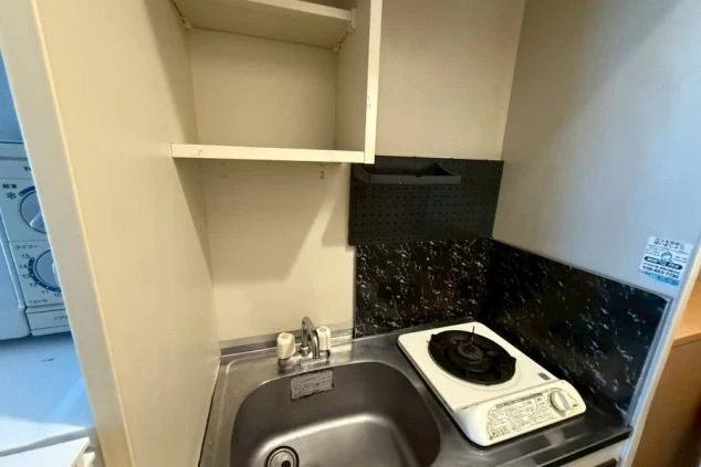 寮のミニキッチン。小さなシンクと一口の卓上ガスコンロが設置されており、上部には収納棚がある。