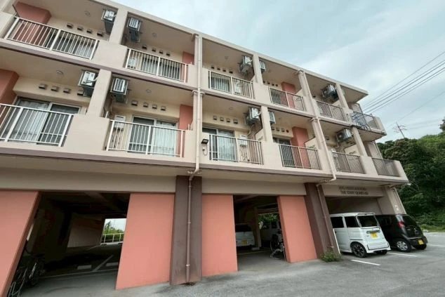 寮の外観。上層階はベージュ、1階はピンクがかった柱と壁の建物で、1階部分は駐車場になっている。