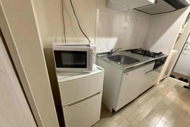 寮のキッチン周り。コンパクトなシンクとコンロが一体となったミニキッチンと、その横に冷蔵庫と電子レンジが設置されている。