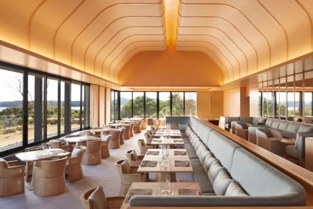 建物の正面。大きな瓦屋根と黒い壁のモダンな和風建築で、全面ガラス戸の向こうに室内が見える。手前は手入れされた芝生で、飛び石がある。