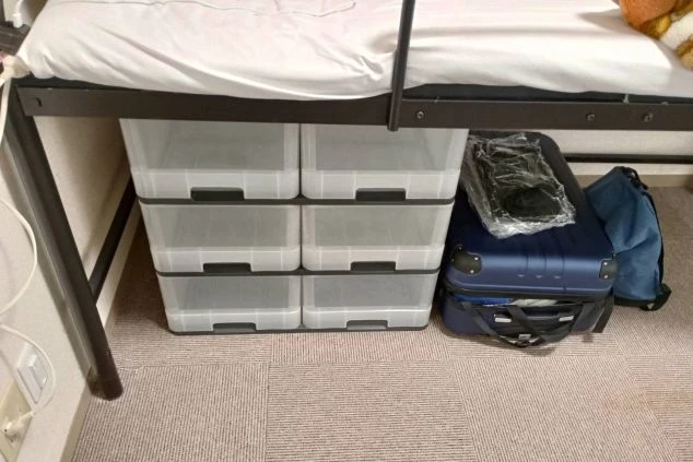 リゾートバイト寮の部屋。ベッドの下に収納ケースとスーツケースが置かれ、荷物を整理できるスペースがある。
