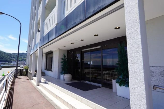 リゾートバイトの仕事先の建物入口を表現するイメージ画像。白を基調としたホテルのエントランスで、ガラス扉の向こうに海が反射して見える。