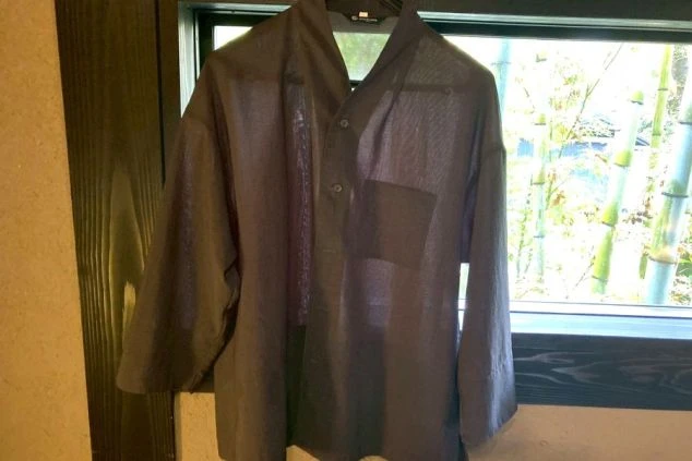 竹林を背景にした窓にハンガーで吊るされた、濃いグレーの長袖の制服。