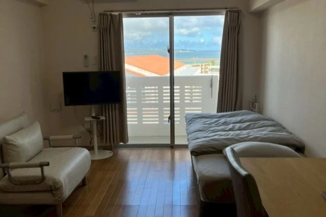 フローリングの床の個室寮。窓からは海が見え、部屋にはベッド、ソファ、テレビ、そしてテーブルが置かれている。