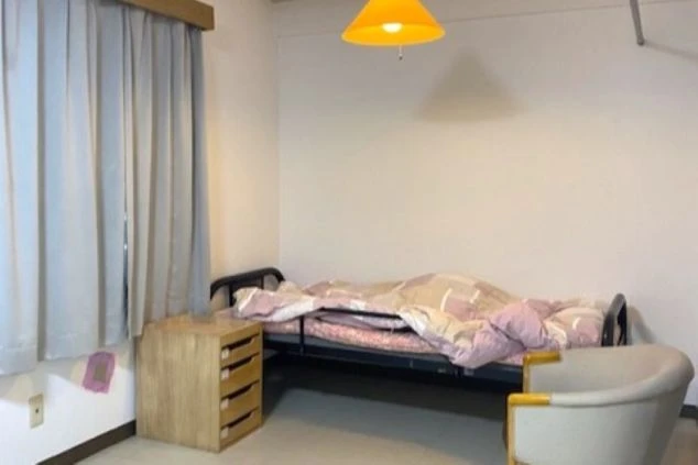 リゾートバイト寮の個室。ベッド、木製のサイドテーブル、アームチェアが備わっており、窓からは自然光が差し込む。