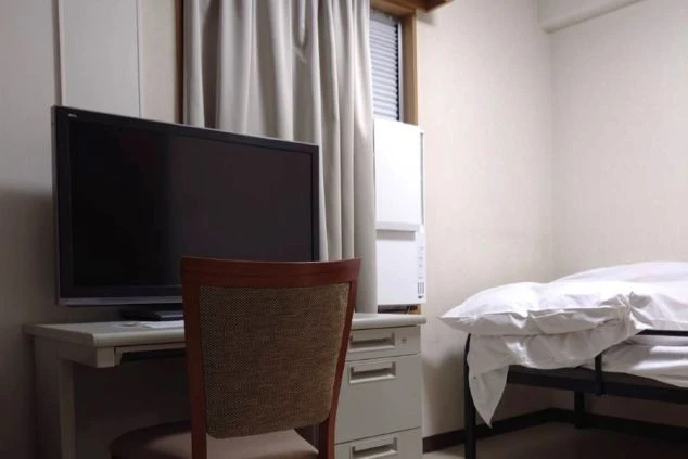 寮の個室の一部。机の上にテレビがあり、ベッドも見える。窓からは柔らかい光が差し込んでいる。