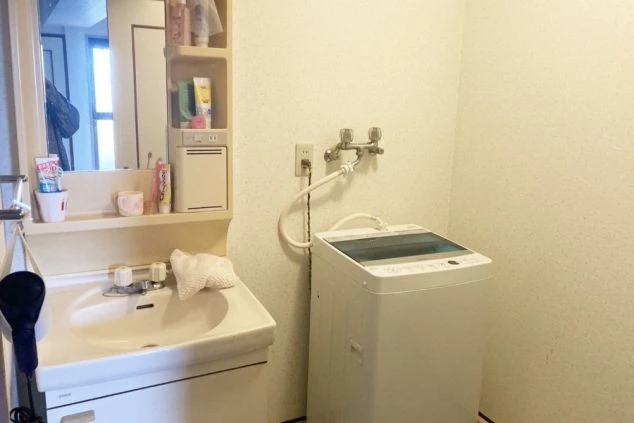リゾートバイト寮の洗面所。洗面台の横に洗濯機が置かれており、身だしなみや洗濯に便利な設備の画像。