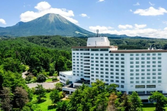 緑豊かな山々に囲まれた、白いホテルの外観の画像。建物はとても大きく、リゾートバイトの仕事場となる、ホテルの外観の画像。